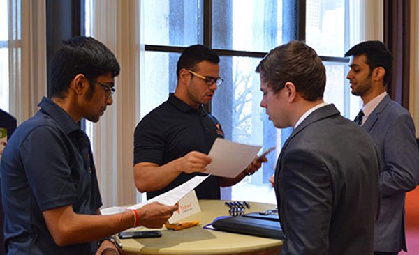Students in business attire, standing around tables talking with employers.