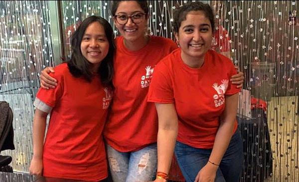 Three young female students smiling with their arms around each other, wearing matching red 