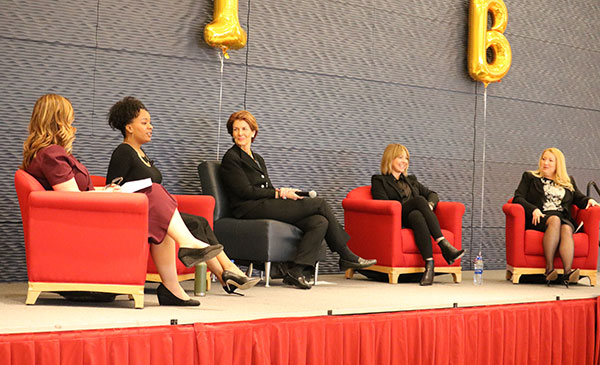 Women on a stage, sitting in chairs, smiling and talking during a panel at the Women in Business conference