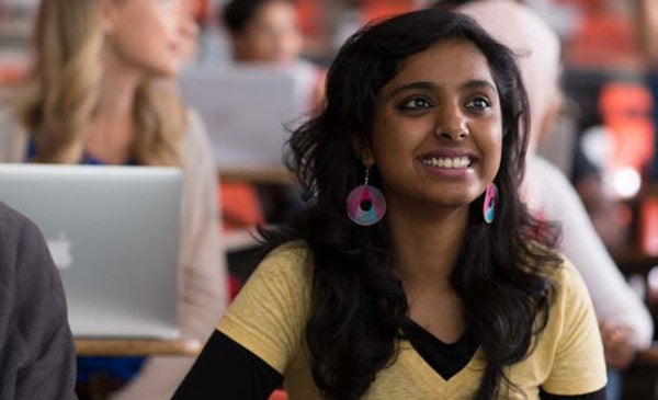 A student sitting in a lecture hall smiling.