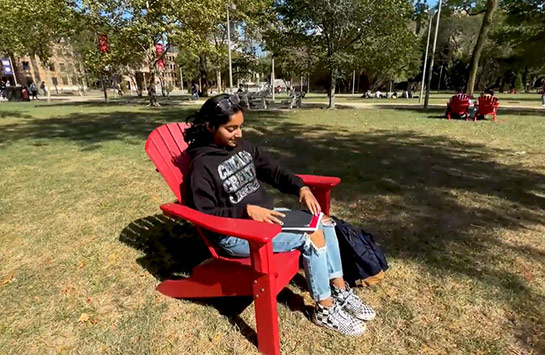 UIC student sitting in a red Adirondack chair on campus